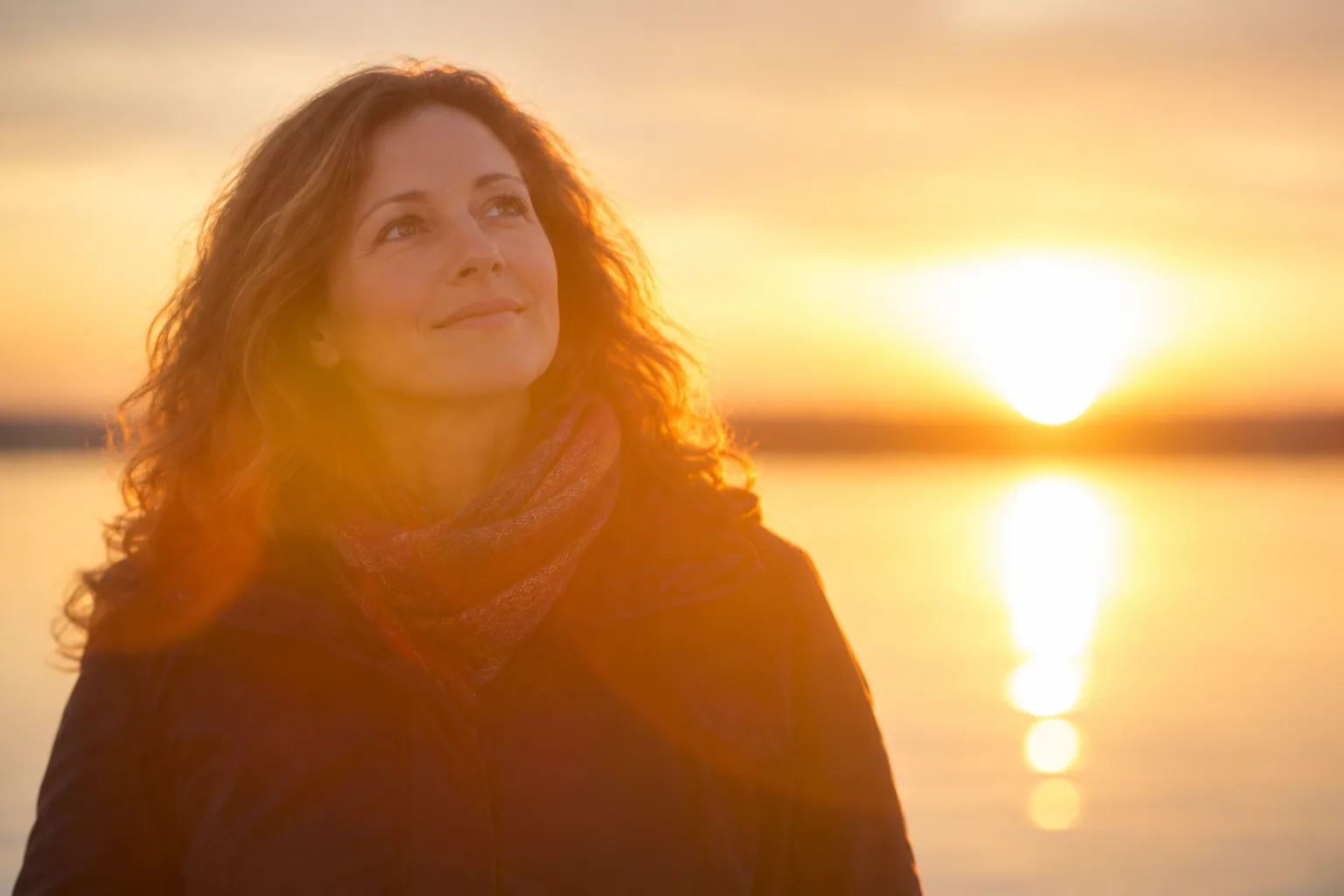 A woman looking toward the sky beside the water at sunset
